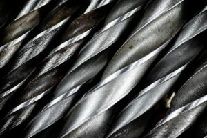 Close-up of several steel twist drill bits arranged diagonally, showing sharp cutting edges and metallic textures.